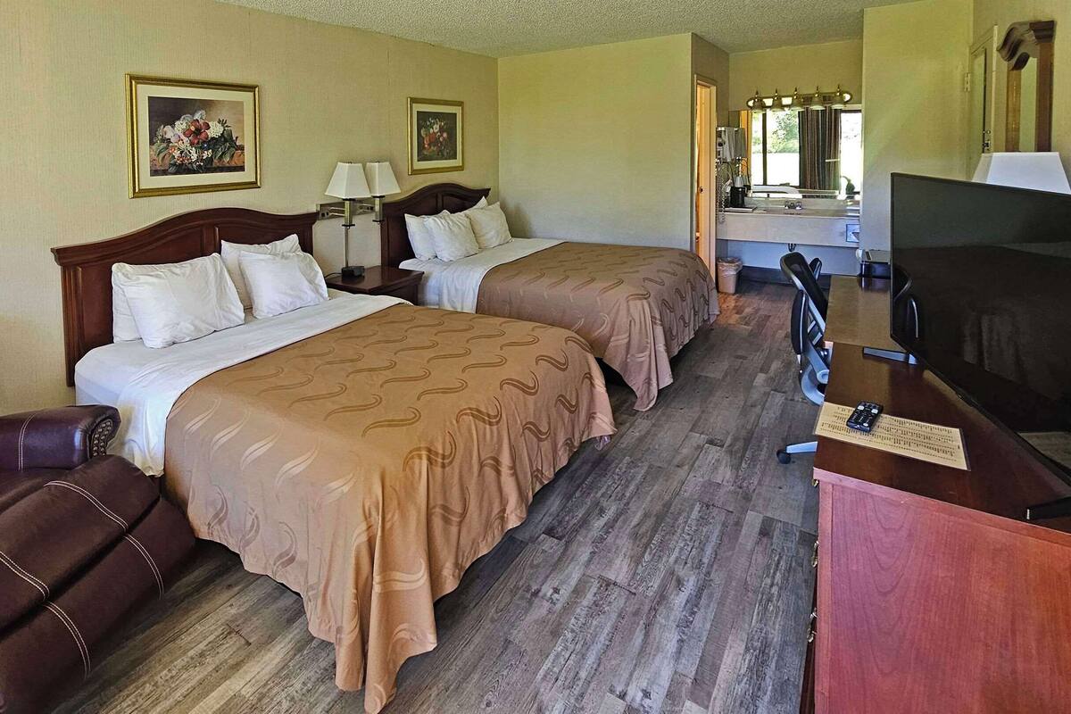 Ein Hotelzimmer mit zwei Betten, einem Fernseher, einem Schreibtisch und einem Stuhl.