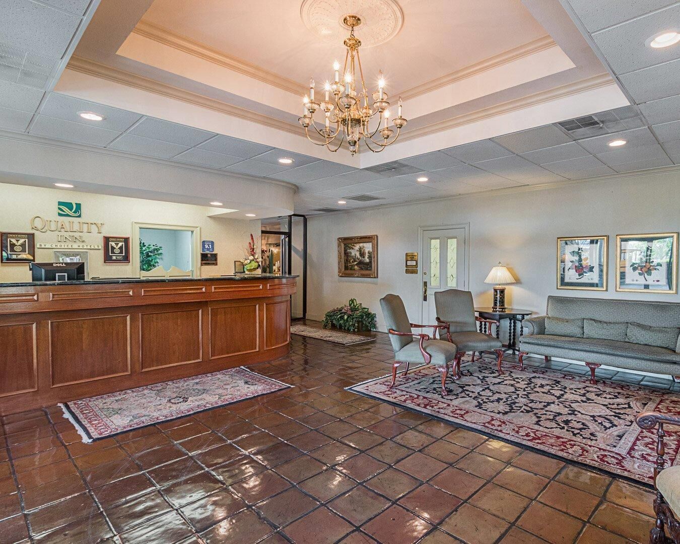 Vestíbulo de hotel con recepción, área de descanso, candelabro y obras de arte.