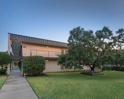 Un edificio moderno con techo plano, una galería techada y un césped cuidado.