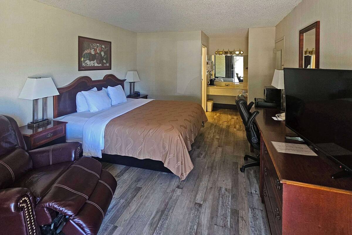 Ein Hotelzimmer mit einem Bett, einem Ledersessel, einem Schreibtisch mit Fernseher und einem Spiegel.