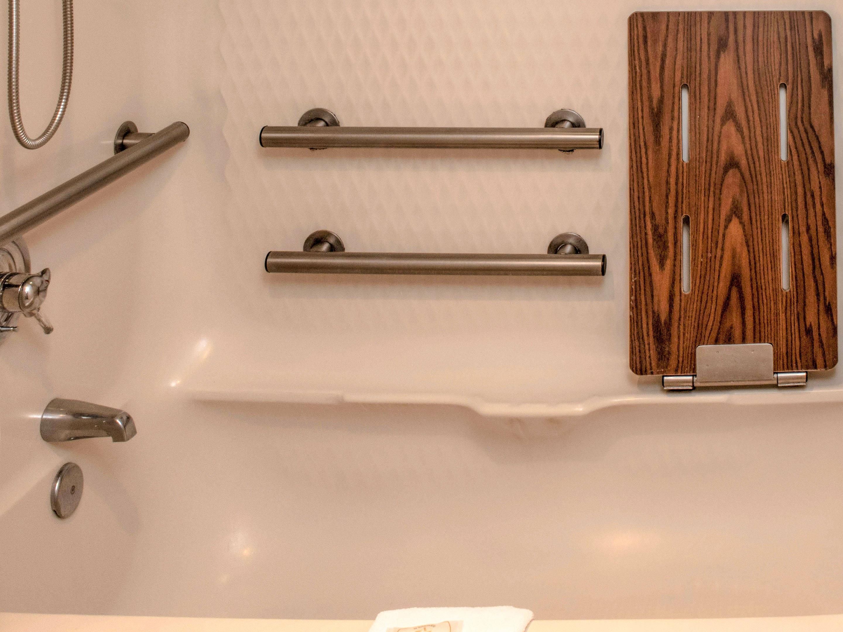A bathroom with a bathtub, two grab bars, a wooden panel, and a towel rack.