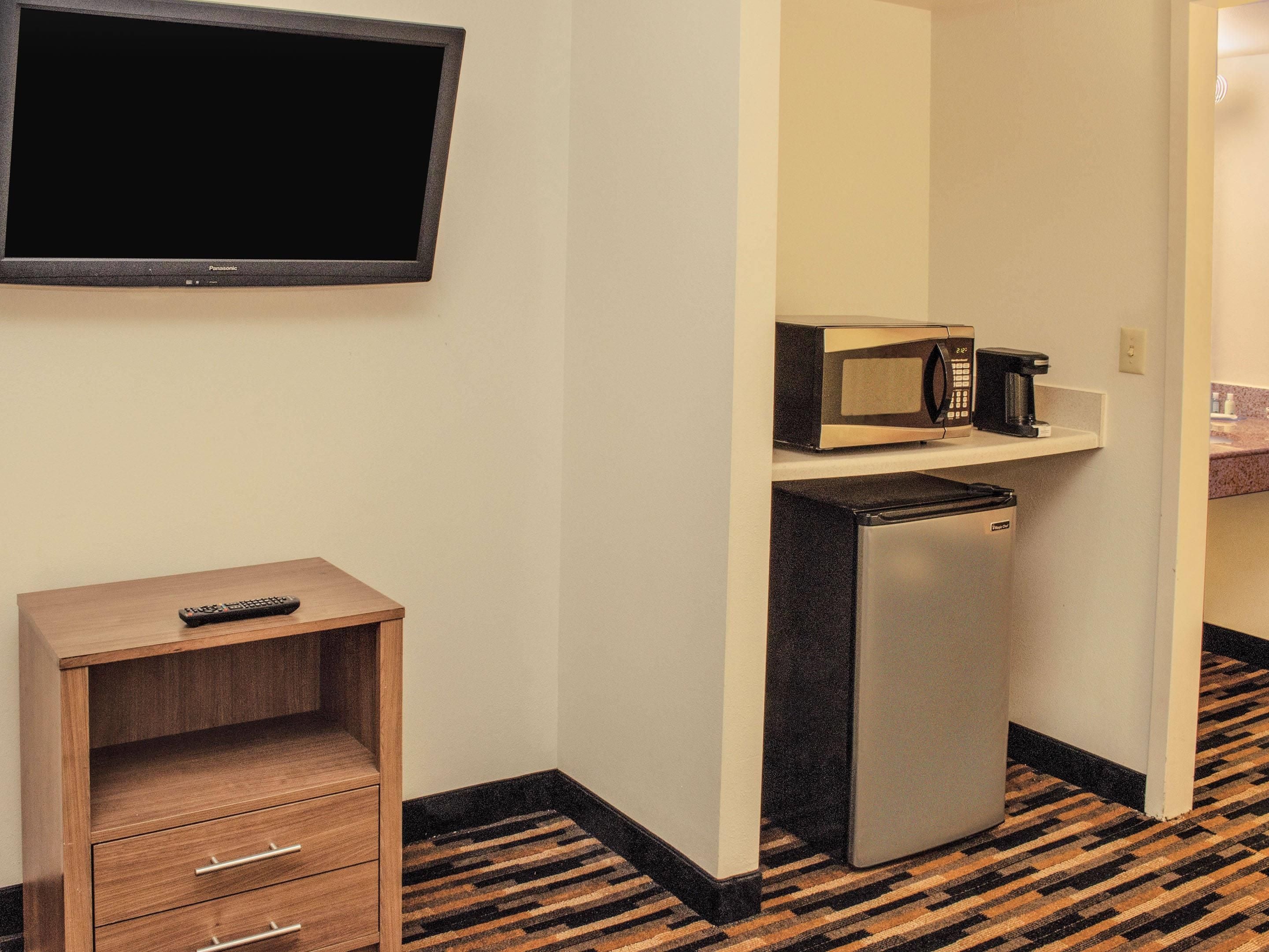 Habitación de hotel con televisor de pantalla plana, microondas, refrigerador y mueble de madera con control remoto.