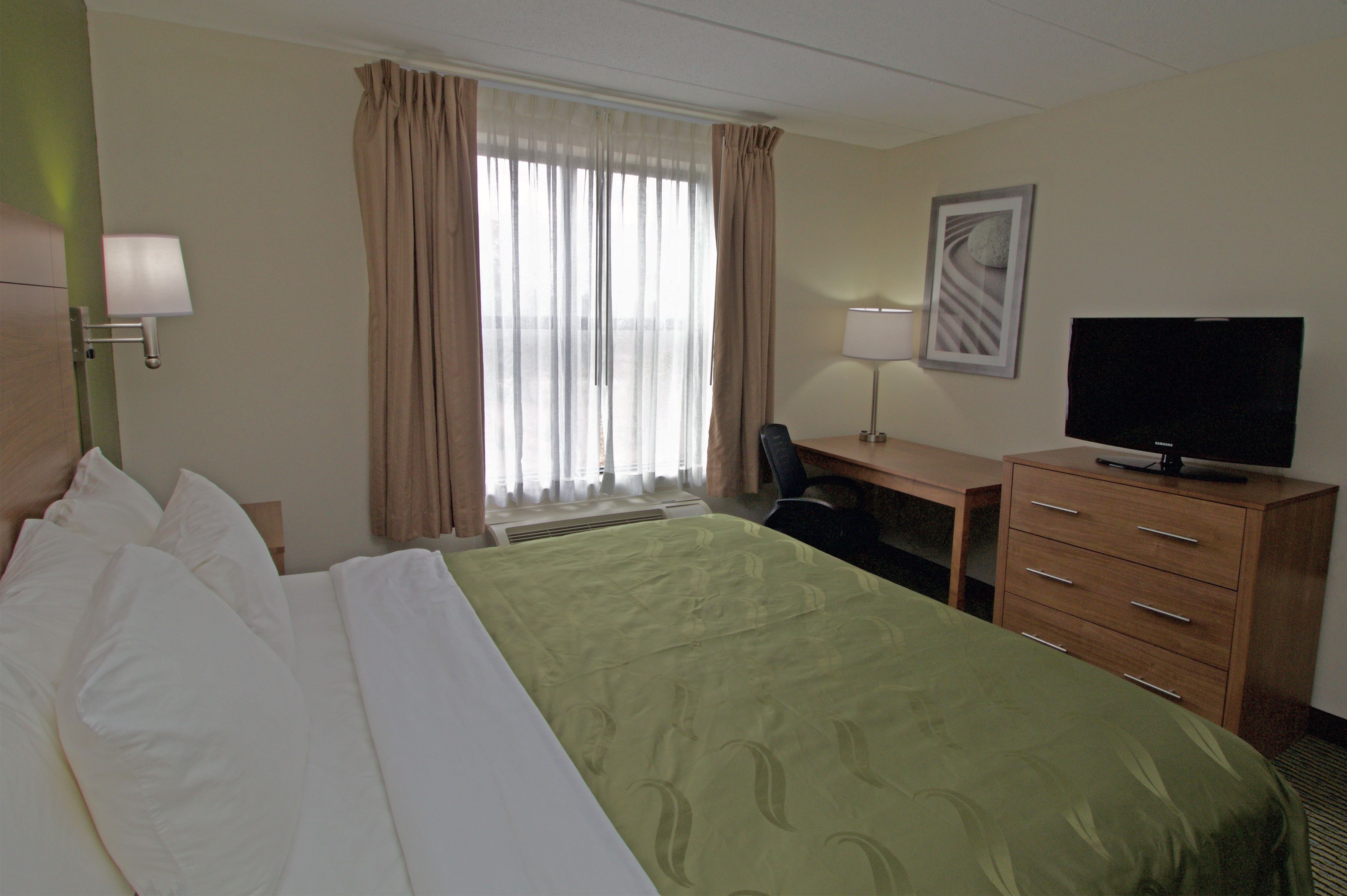 A hotel room with a bed, a desk, a chair, a television, and a window with curtains.