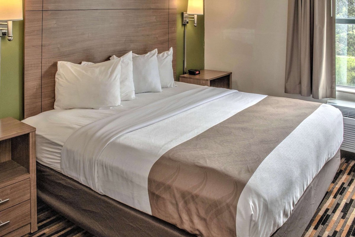 Una habitación de hotel con una cama grande, dos mesitas de noche, una lámpara y una ventana con cortinas.
