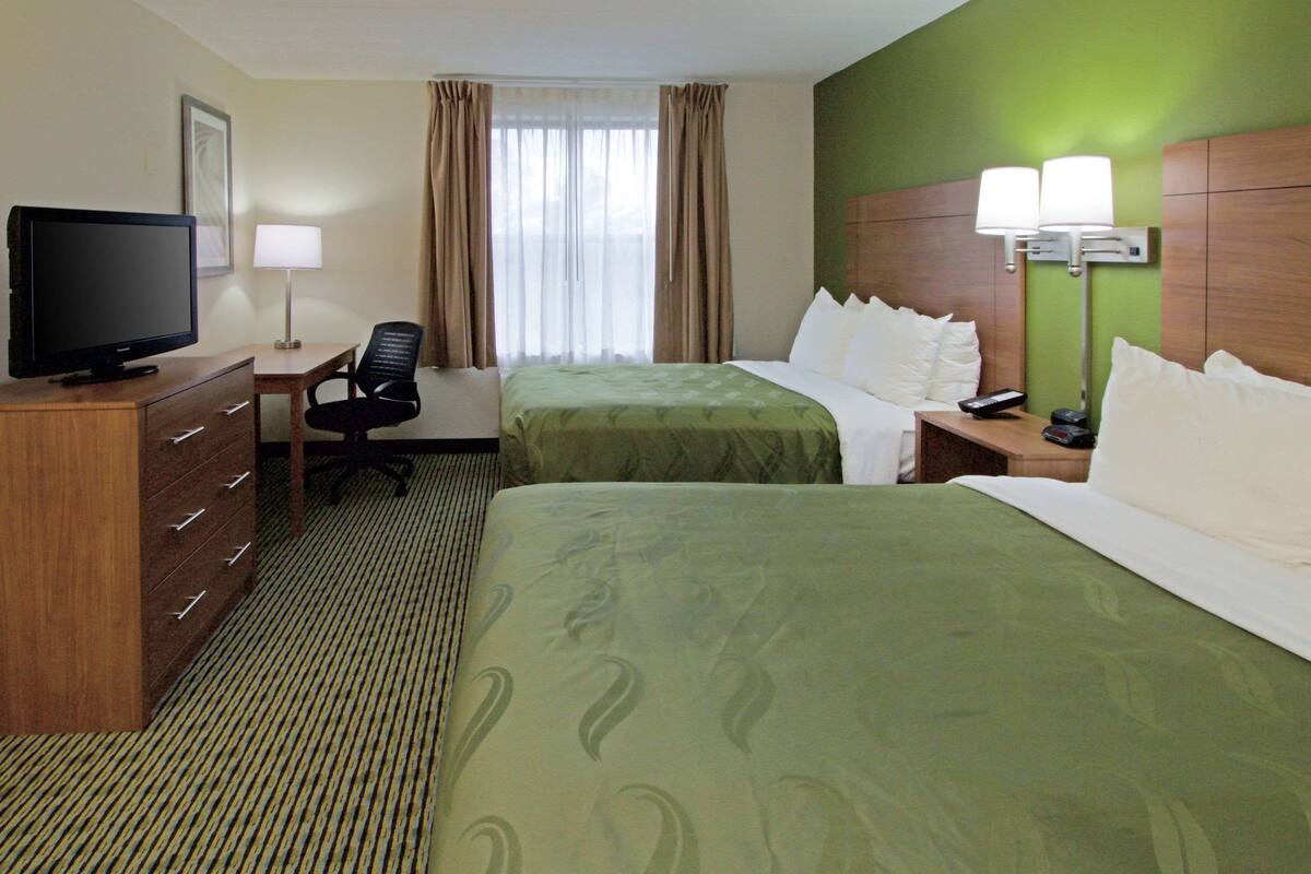 A hotel room with two beds, a desk, a television, a chair, and a lamp.