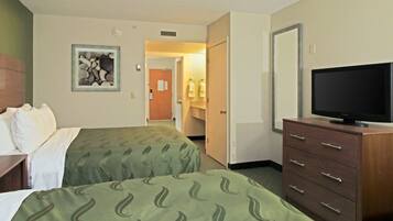 Una habitación de hotel con dos camas, un televisor sobre una cómoda y un baño visible a través de una puerta abierta.