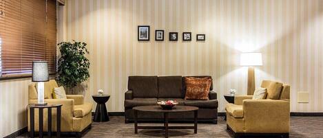 A hotel lobby with a striped wall, a sofa, two armchairs, a coffee table, a lamp, a plant, and framed pictures.