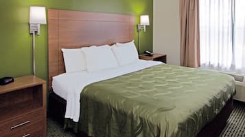 A hotel room with a wooden headboard, a green bedspread, two bedside lamps, a nightstand, and a window with curtains.
