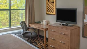 Habitación de hotel con cama, escritorio con computadora, silla, cómoda y ventana con vista a árboles.