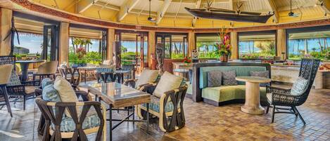 A spacious indoor area with high ceilings, large windows, and a variety of seating arrangements including sofas, chairs, and tables.