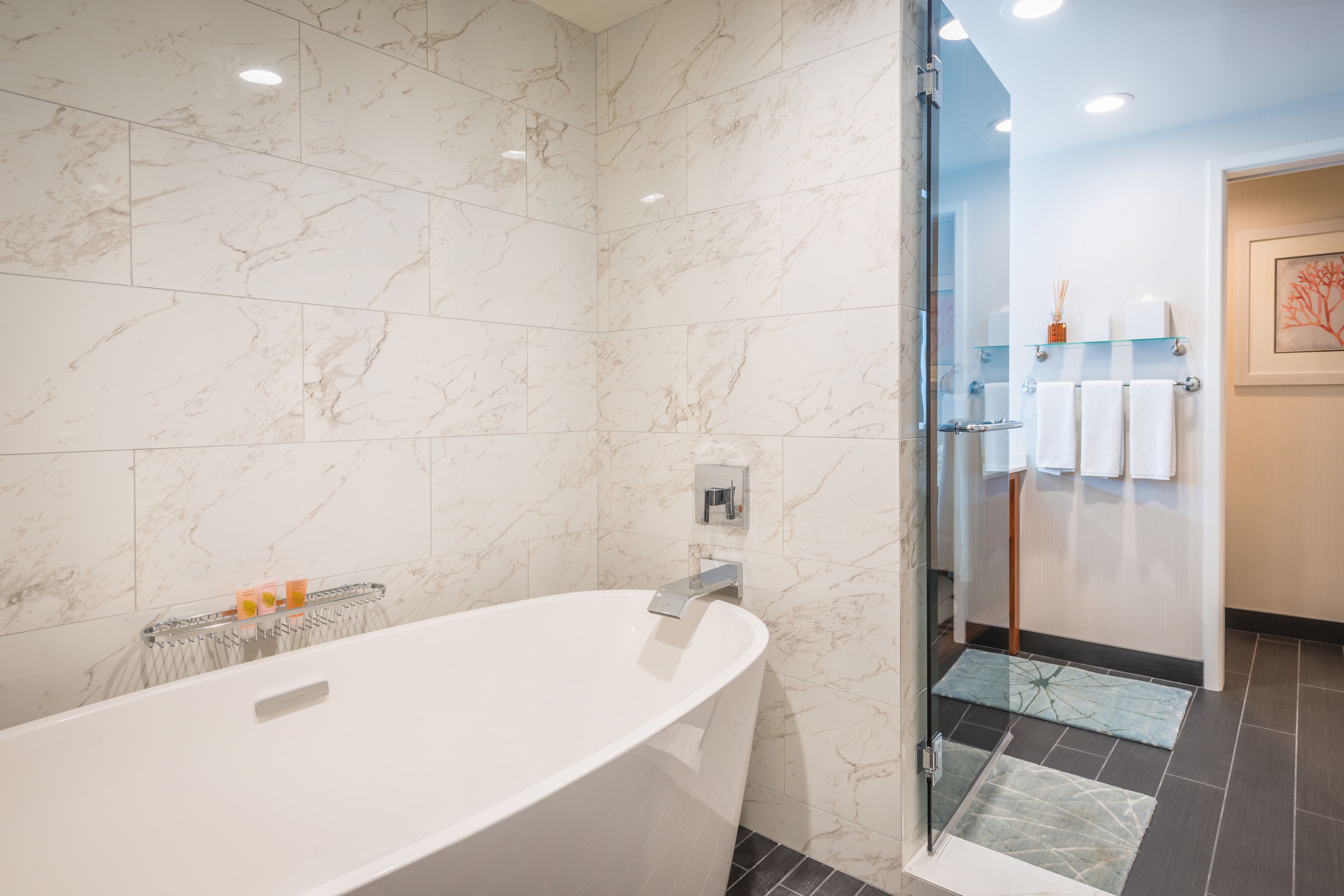 Un baño moderno con una bañera independiente, baldosas de mármol, cabina de ducha de vidrio y un perchero con toallas blancas.