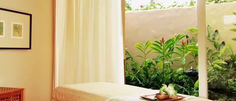 A room with a bed, a ceiling fan, a window with curtains, and a view of greenery outside.