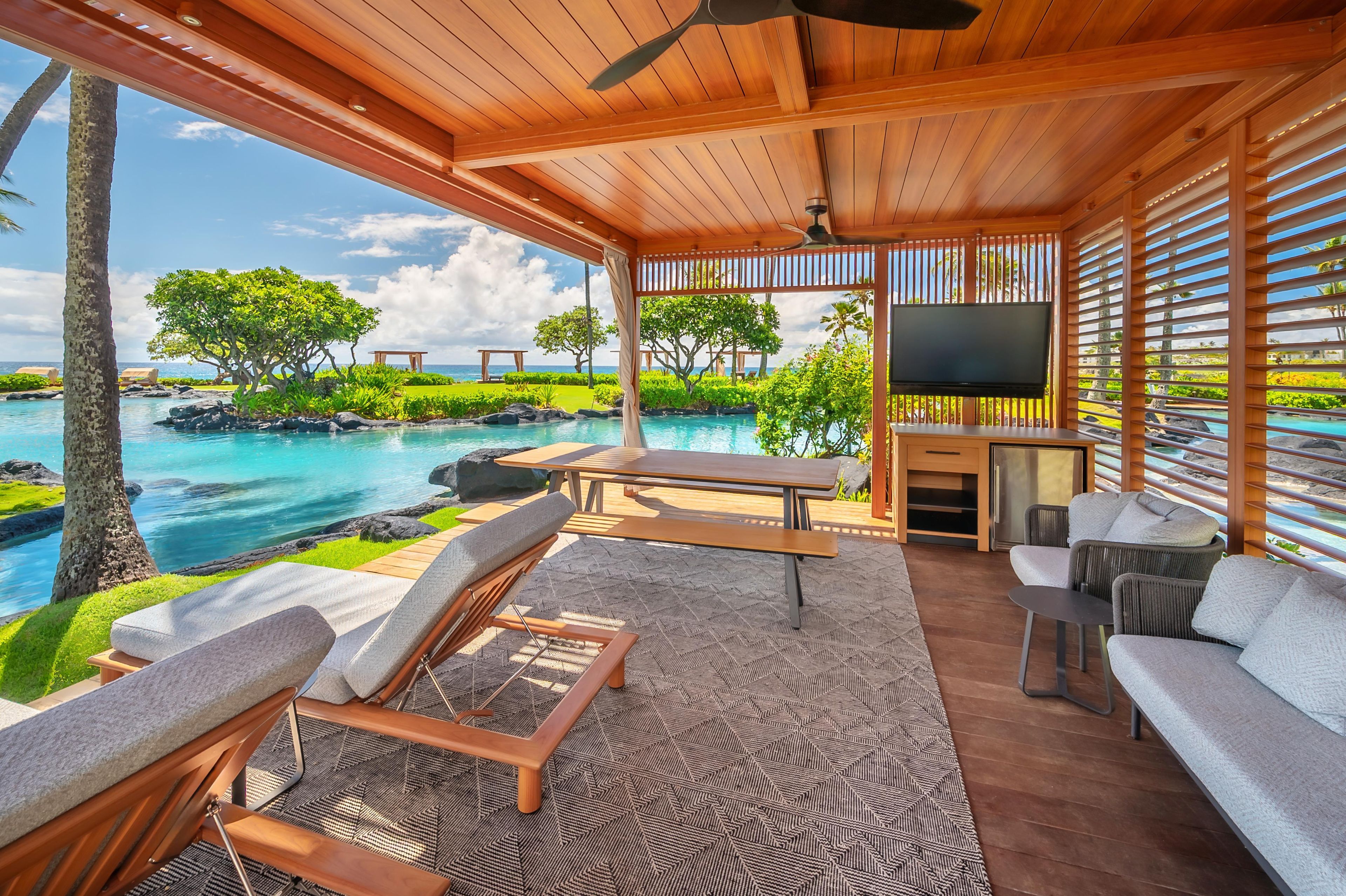 A covered outdoor seating area with a pool view, wooden furniture, and a flat-screen TV.