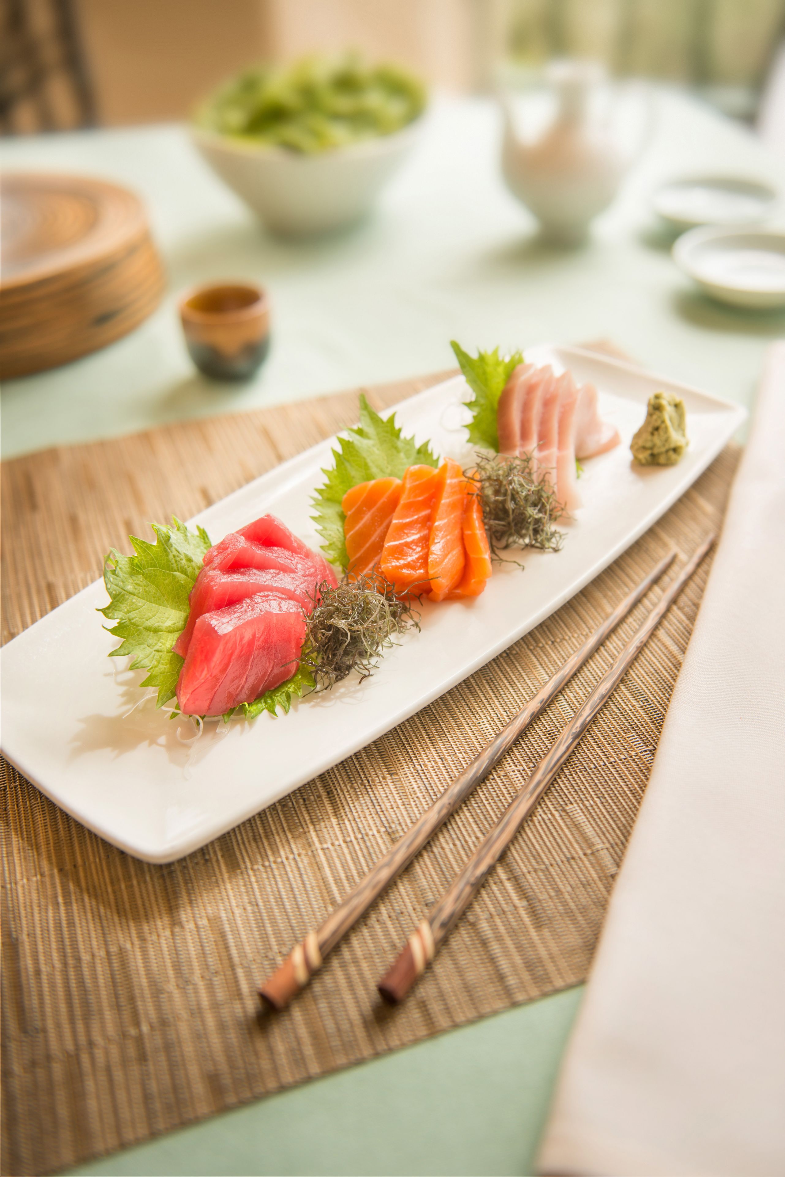 A sushi platter on a rectangular white plate with chopsticks beside it, placed on a bamboo mat.