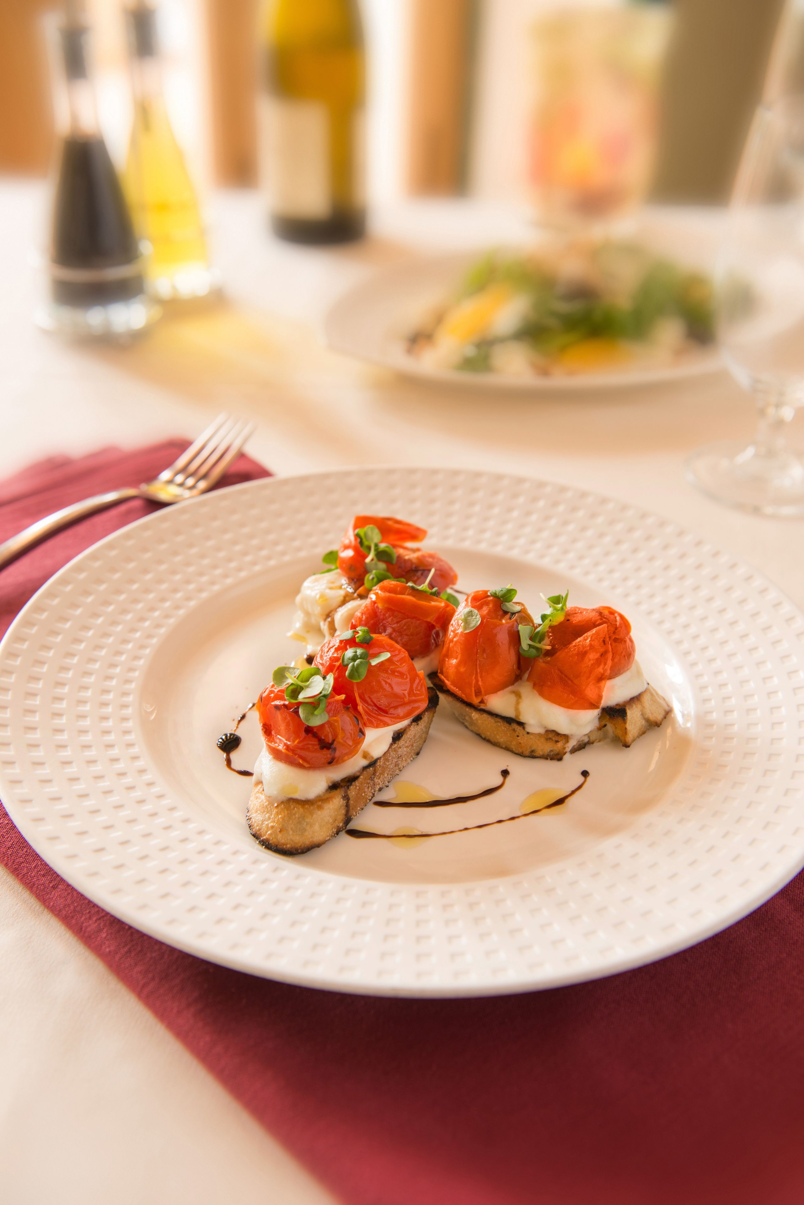 A plate of bruschetta with tomatoes and greens on a white plate.