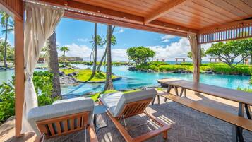 A covered outdoor seating area with a view of a pool and tropical landscape.