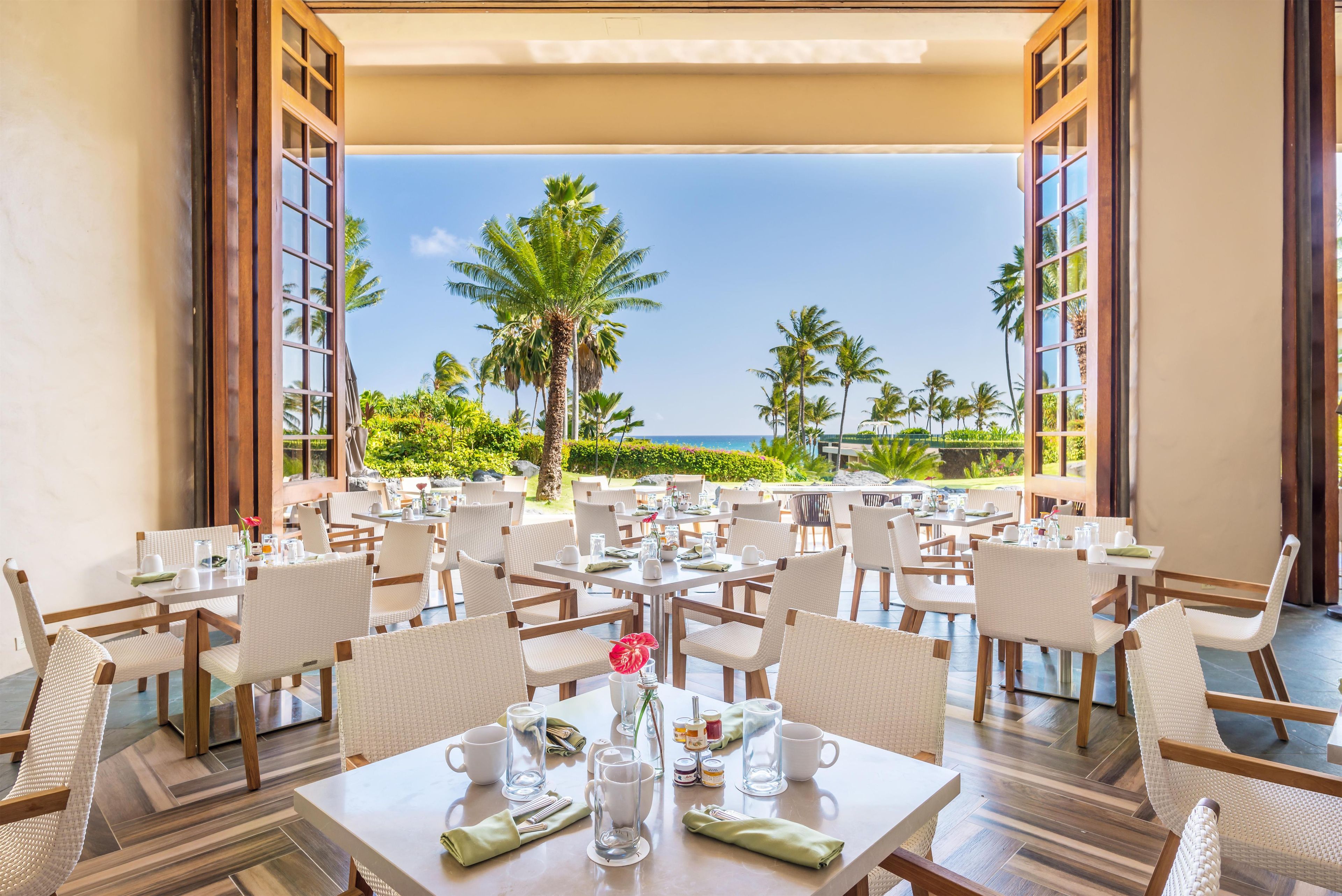 Een restaurant met terras aan het strand, met tafels en stoelen klaar voor een maaltijd.
