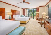 A hotel room with two beds, a desk, a chair, a television, and a balcony with a view of palm trees.