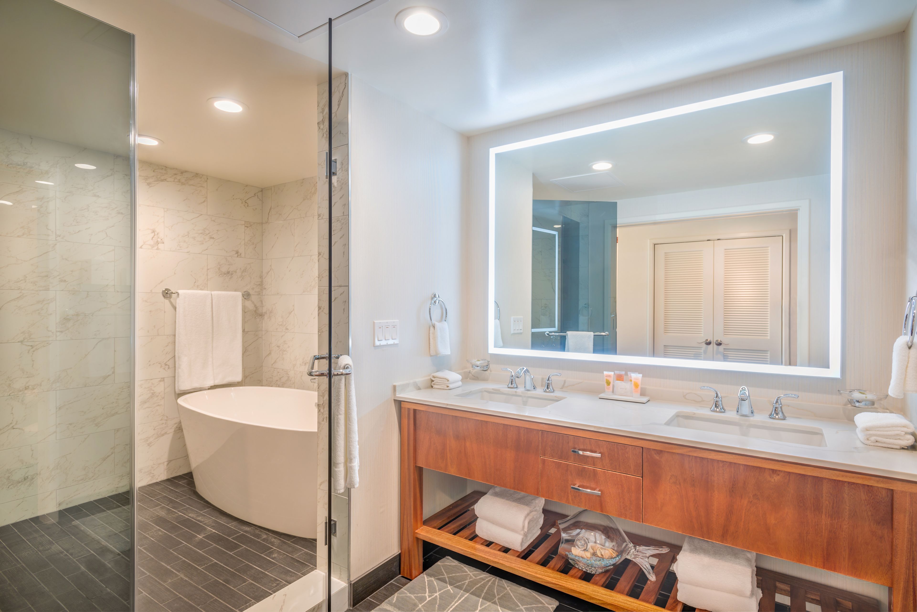A modern bathroom with a glass-enclosed shower, a freestanding bathtub, a large mirror, and a wooden vanity with a sink and countertop.