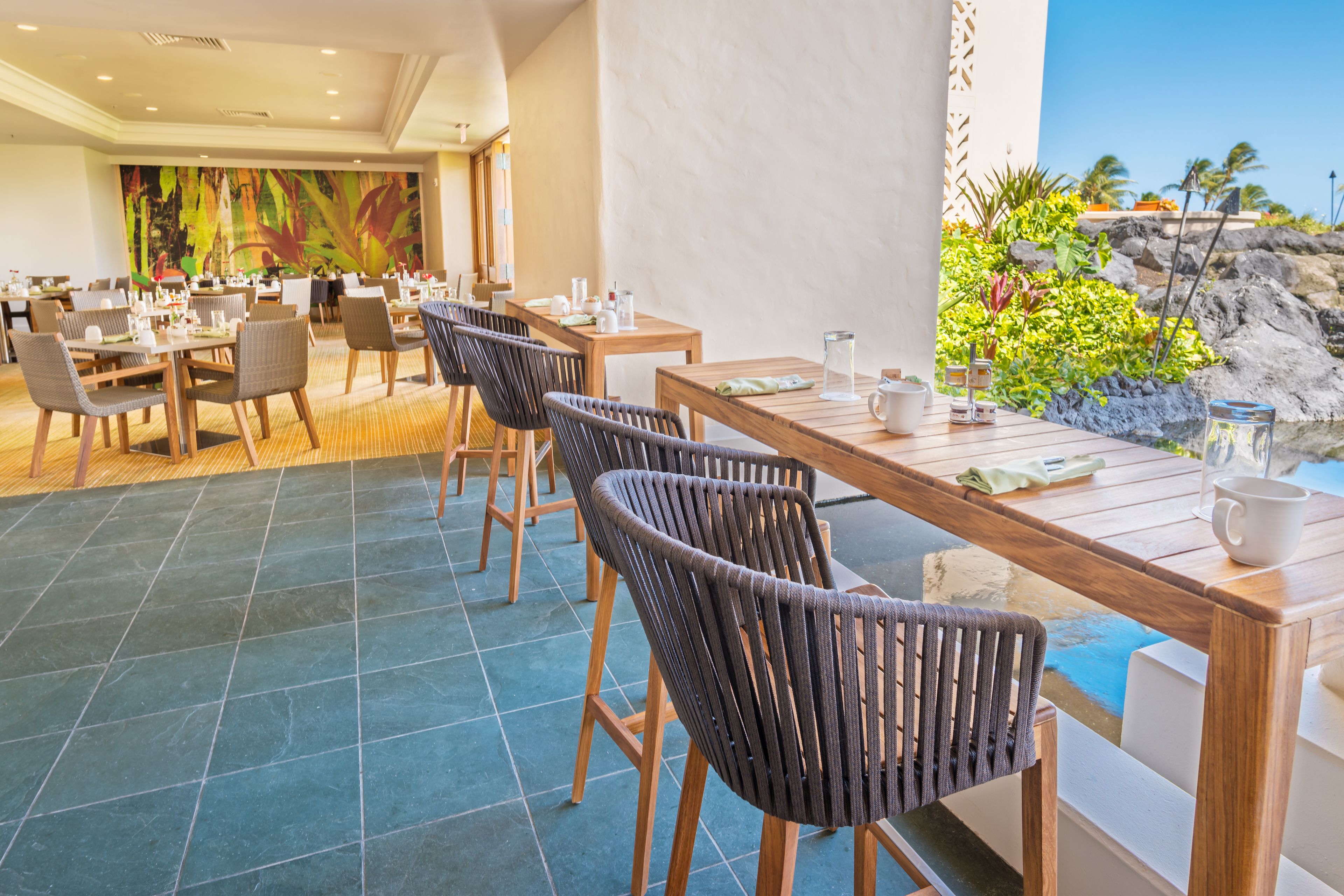 Un restaurante con mesas y sillas de madera, un mural grande en la pared y vista al océano.