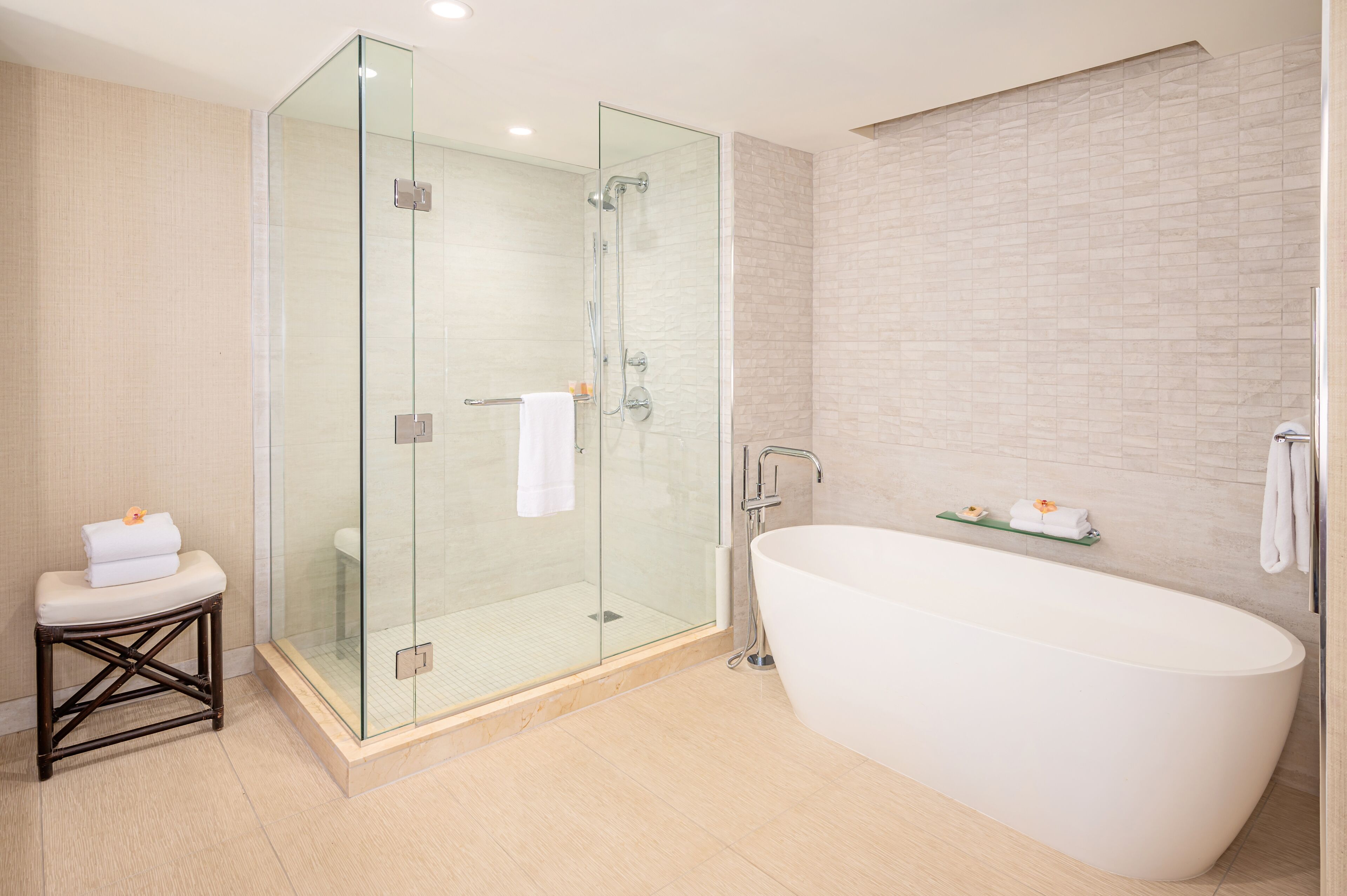 A modern bathroom with a glass-enclosed shower, a freestanding bathtub, and a small stool with towels.