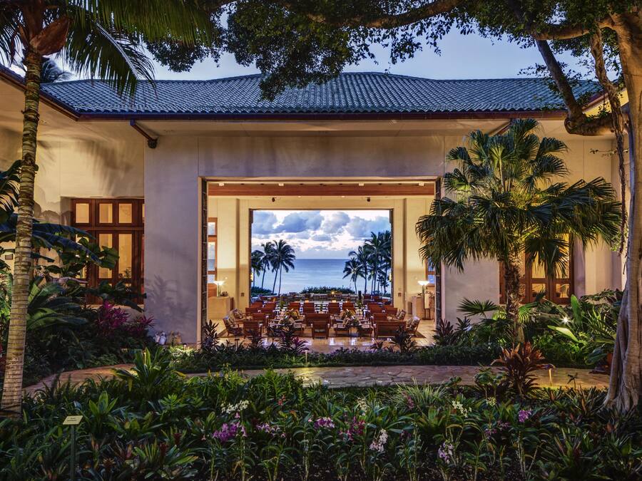 A hotel lobby with a view of the ocean, palm trees, and a seating area.