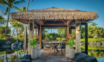A bar area with a long counter, multiple chairs, and a view of palm trees through large windows. at Grand Hyatt Kauai Resort and Spa