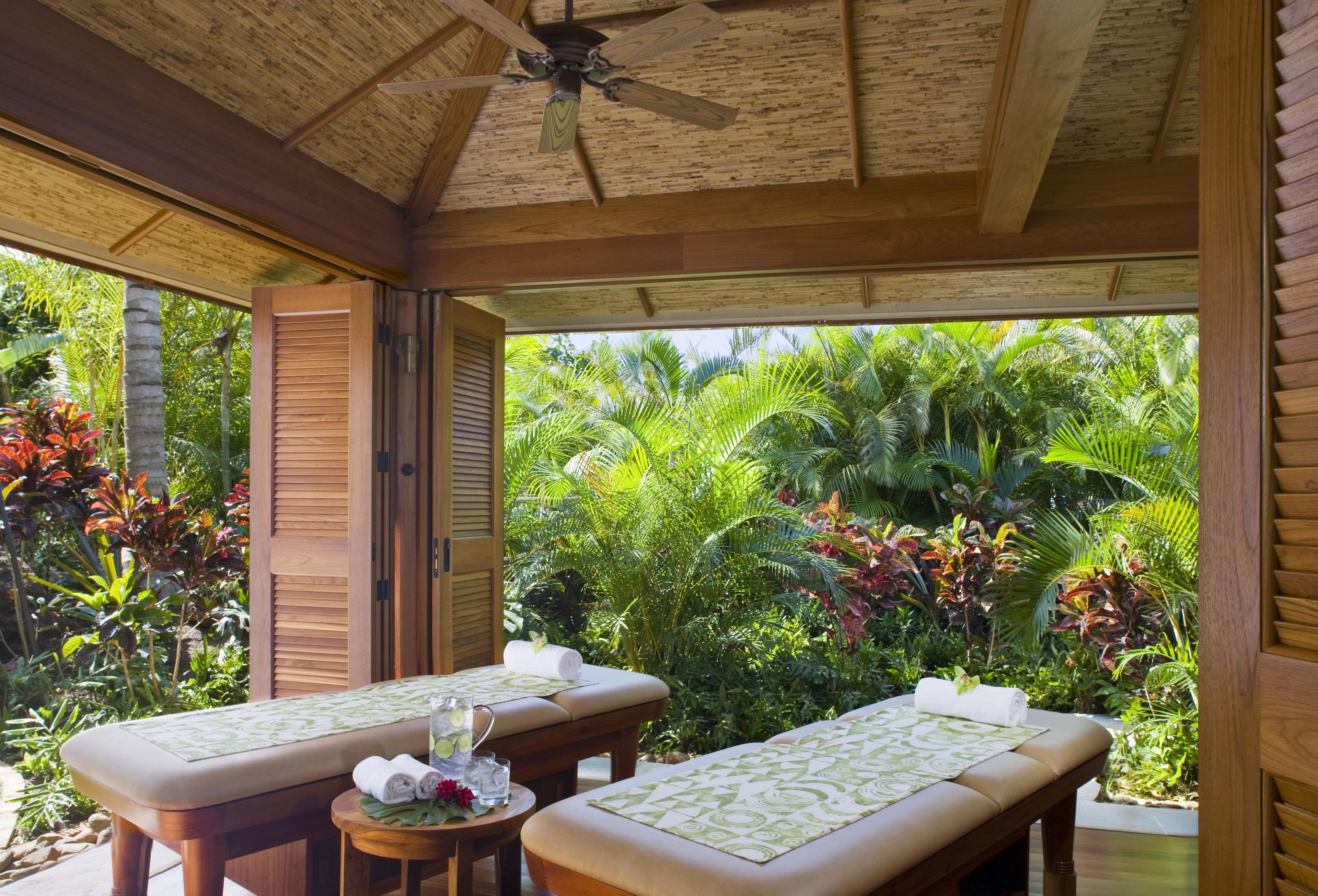 Une pièce en bois avec deux tables de massage, un ventilateur de plafond et une vue sur une végétation tropicale luxuriante.