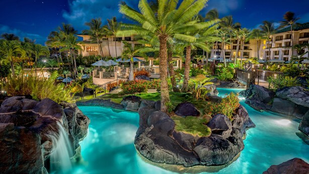 Zona de piscina en un resort con agua cristalina, palmeras y cielo nocturno.