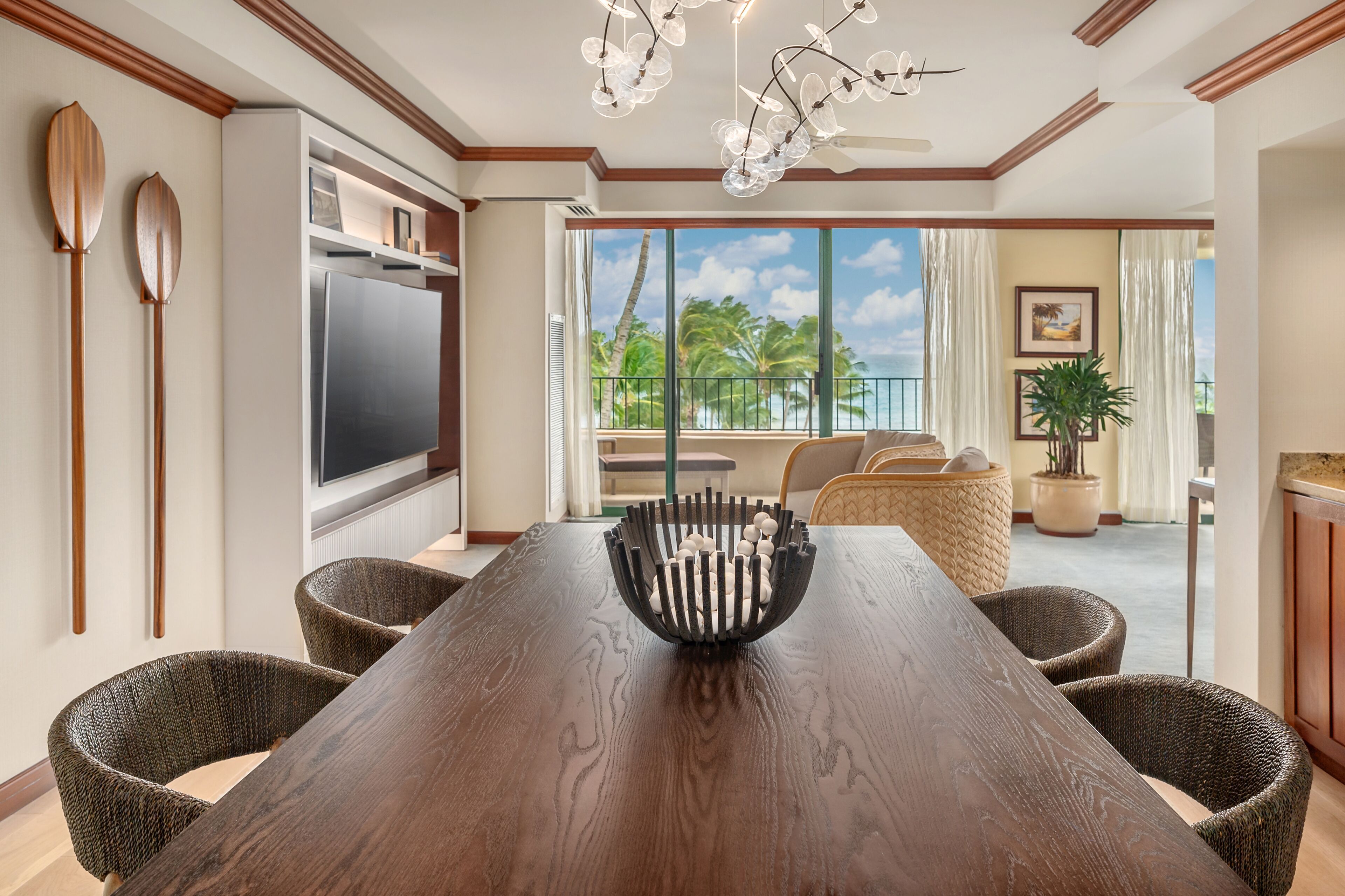 A dining area with a wooden table, wicker chairs, a modern chandelier, and a view of the outdoors.