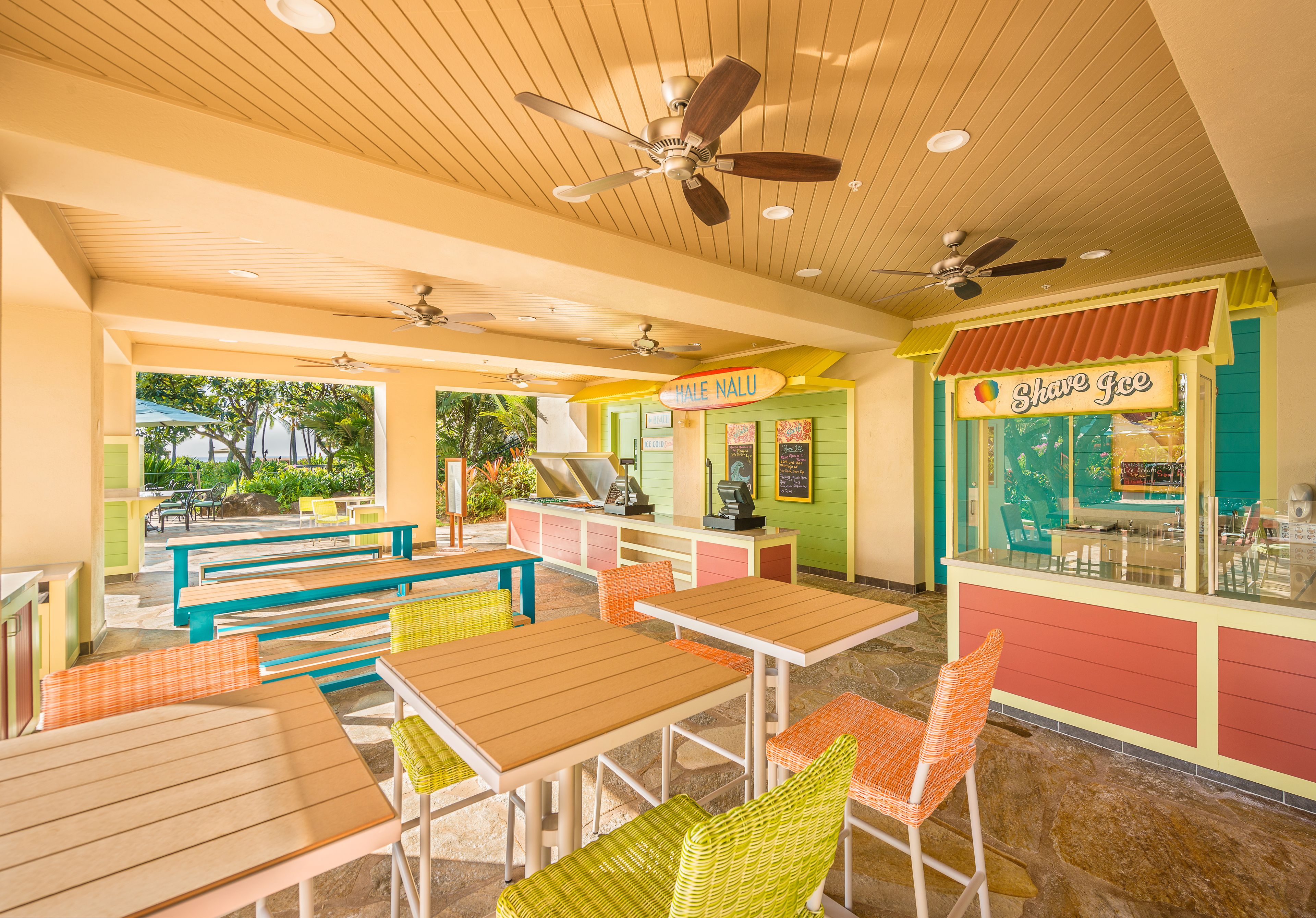 Un restaurante interior con mesas y sillas de madera, ventiladores de techo y una barra con un letrero que dice 'Shave Ice'.