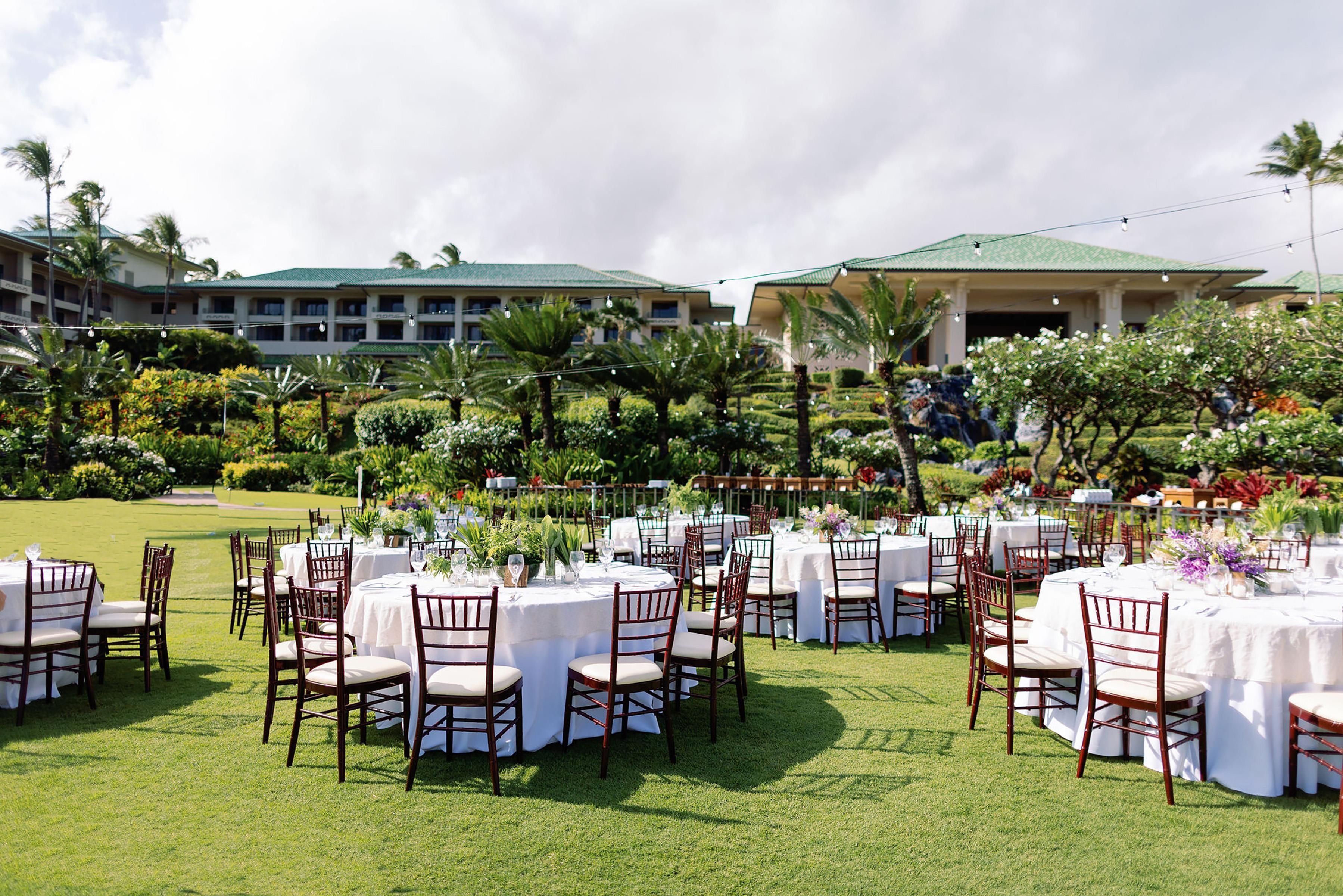 Un espace de restauration en plein air avec des tables et des chaises rondes, entouré d’une végétation luxuriante et de palmiers.