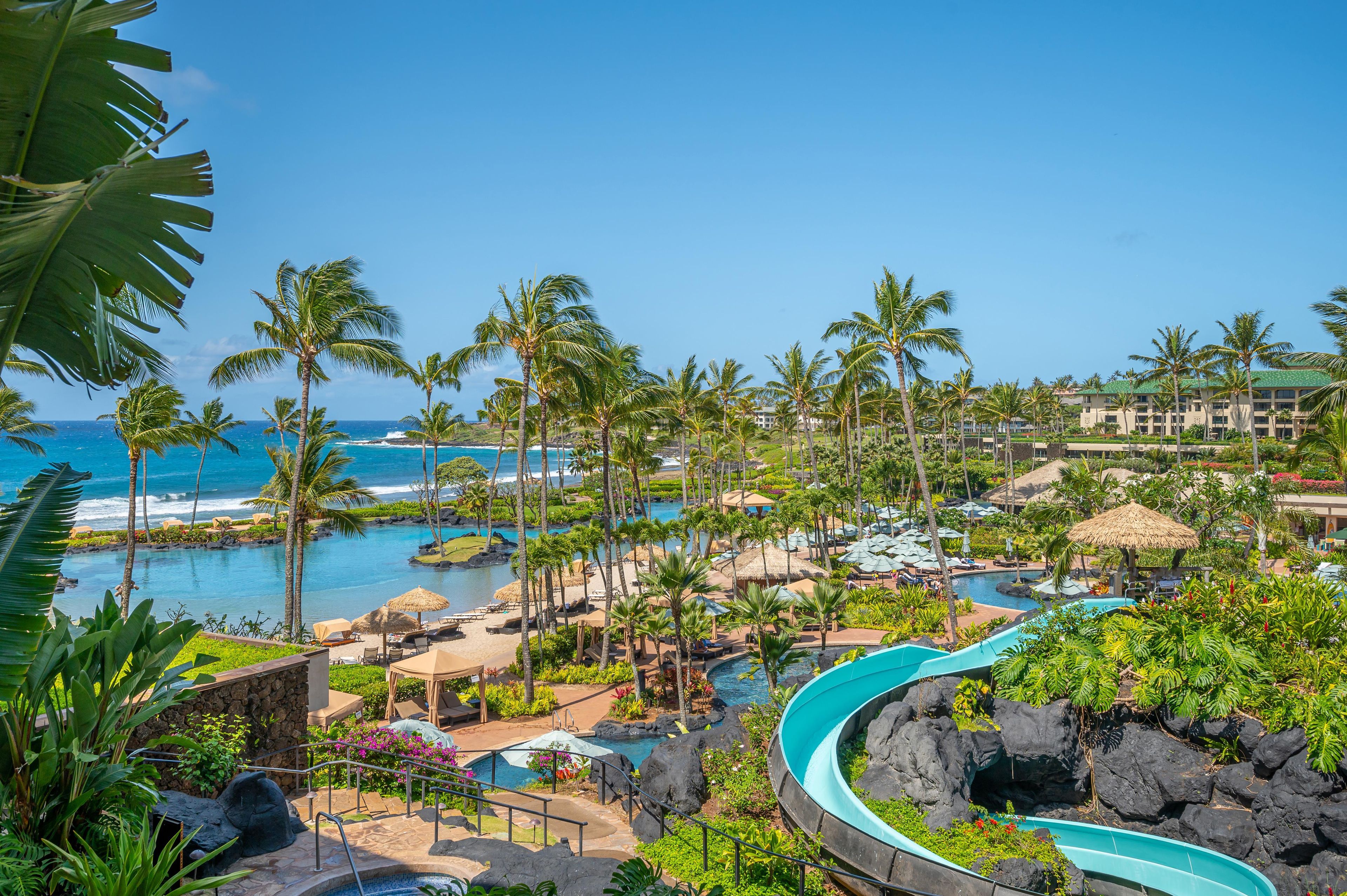 A resort with multiple swimming pools, palm trees, and a view of the ocean.