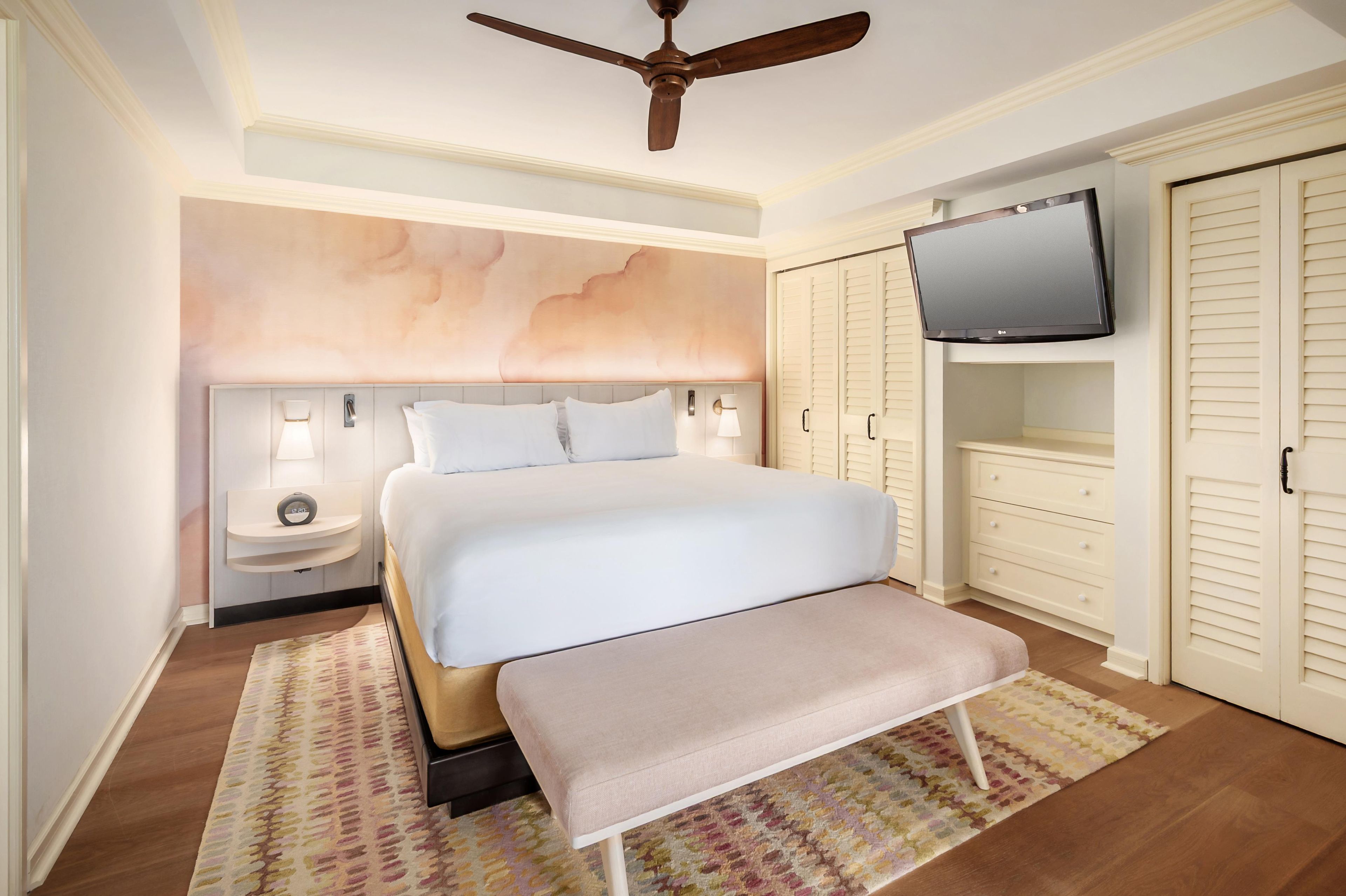 A hotel room with a bed, bedside tables, a television, and a wardrobe.
