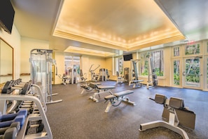 A gym with various exercise equipment, large windows with a view of greenery, and a ceiling with recessed lighting.