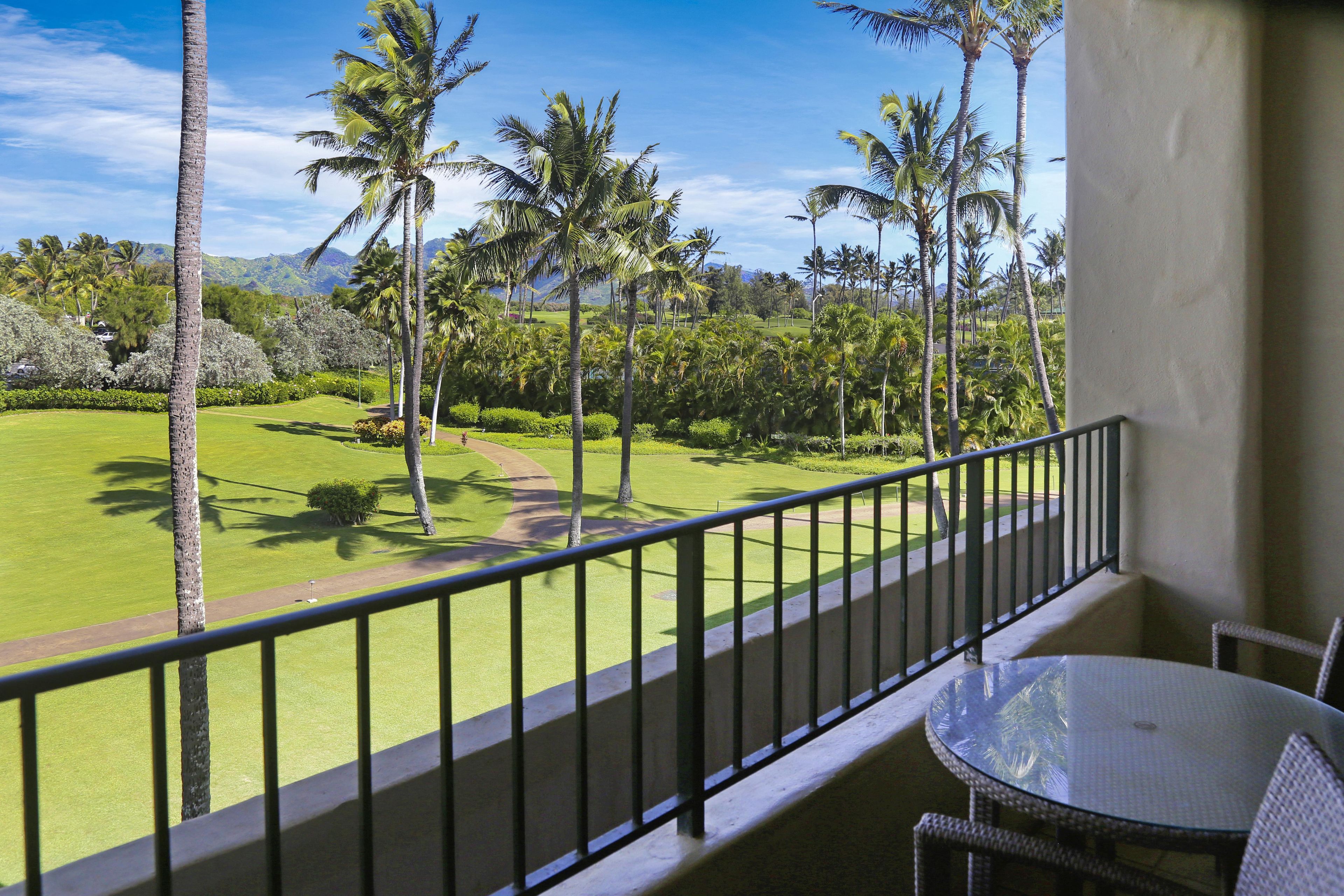 A balcony with a view of a golf course, palm trees, and a mountain in the distance.