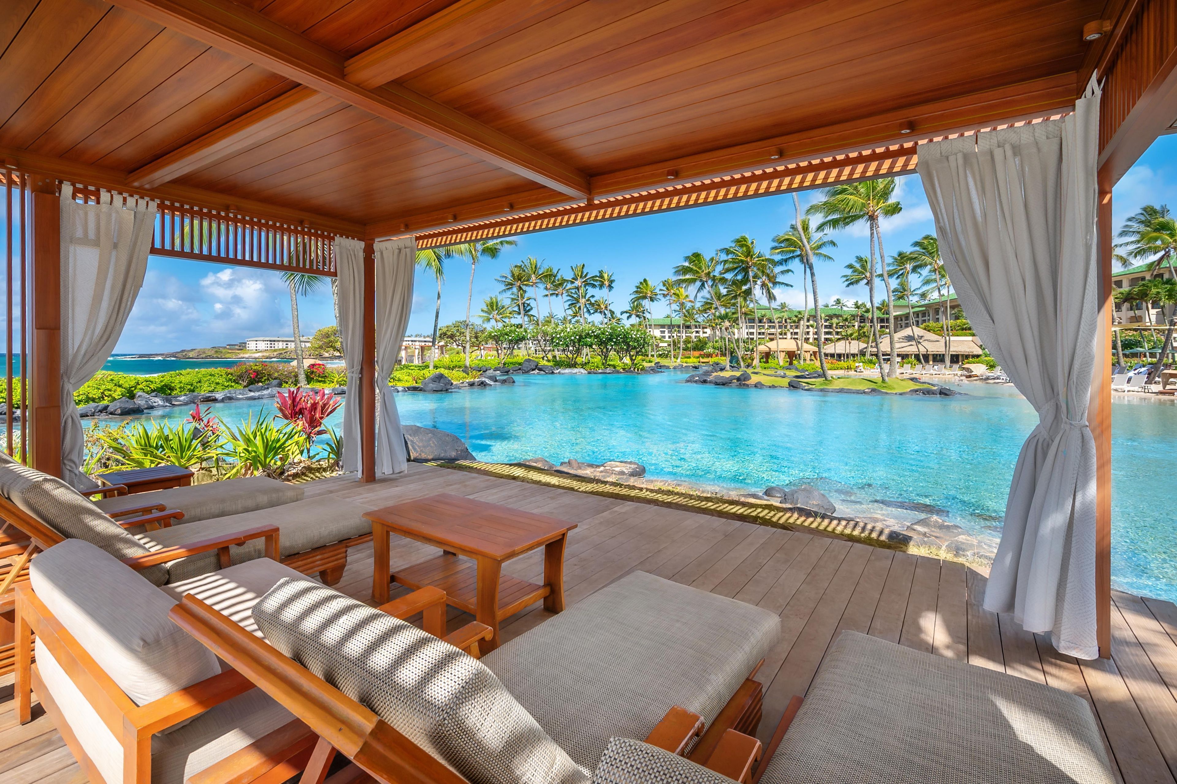 Un espacio de estar techado al aire libre con vistas a una piscina y un paisaje tropical.