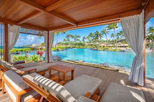 Un espacio de estar techado al aire libre con vistas a una piscina y un paisaje tropical.