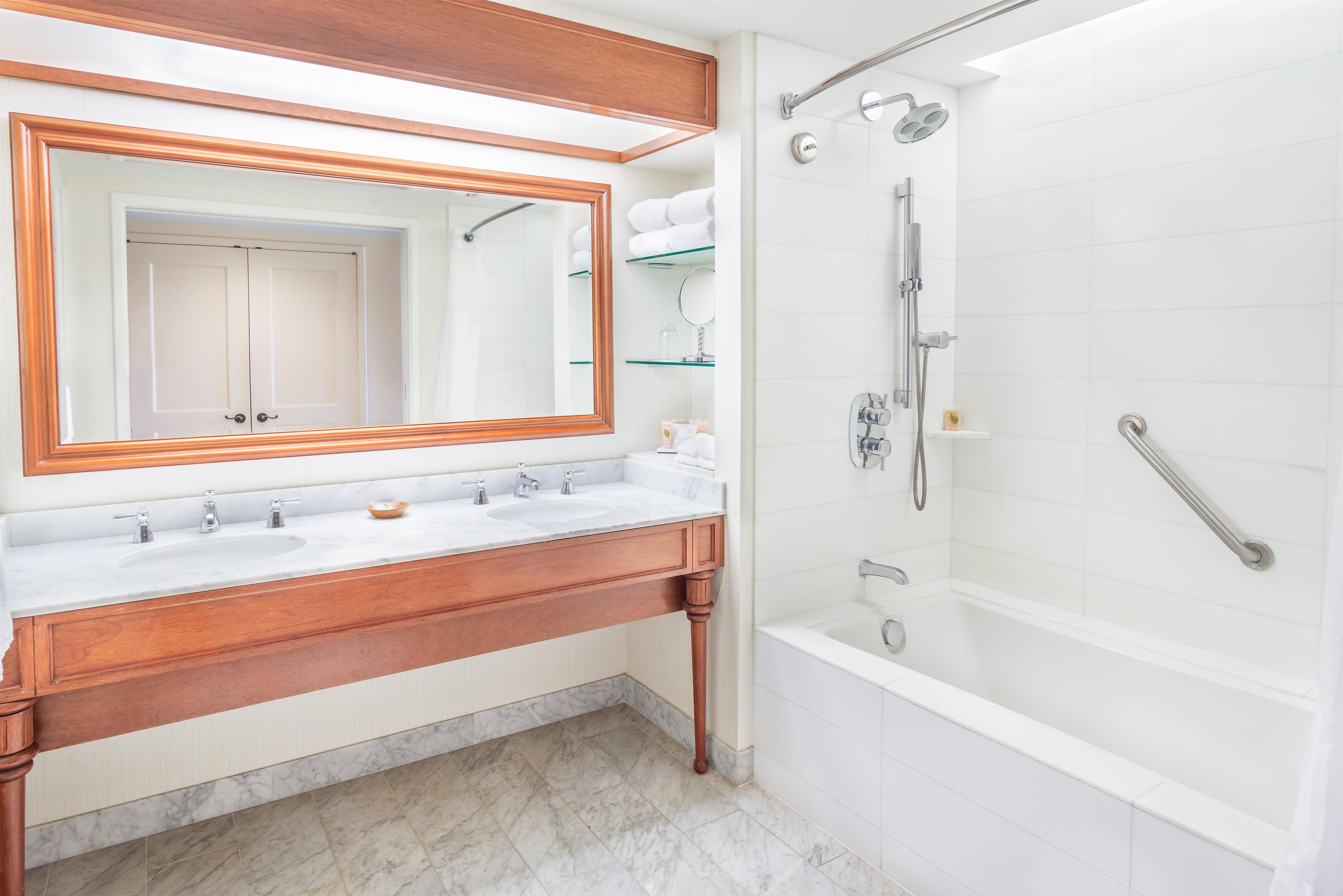 A bathroom with a wooden vanity, a large mirror, a bathtub, and a shower area.
