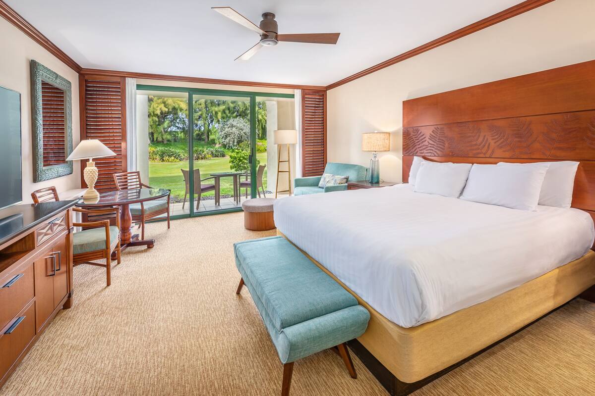 Une chambre d’hôtel dotée d’un grand lit, d’un bureau avec une chaise, d’un banc, d’un ventilateur de plafond et offrant une vue sur l’extérieur.