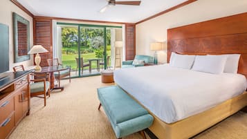 Habitación de hotel con una cama grande, un escritorio con una silla, un banco, un ventilador de techo y vistas al exterior.