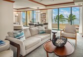 A spacious living room with a large sofa, a coffee table, and a view of the ocean through large windows.