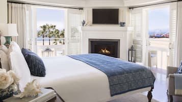 Quarto com cama grande, lareira, televisão e varanda com vista para a praia e uma roda gigante.