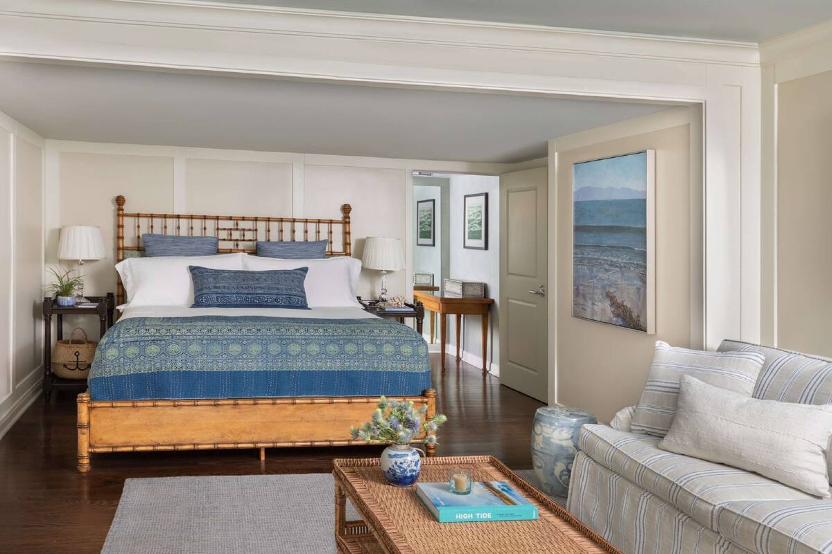 A bedroom with a large bed, a bedside table, a nightstand, a sofa, a coffee table, and a painting on the wall.