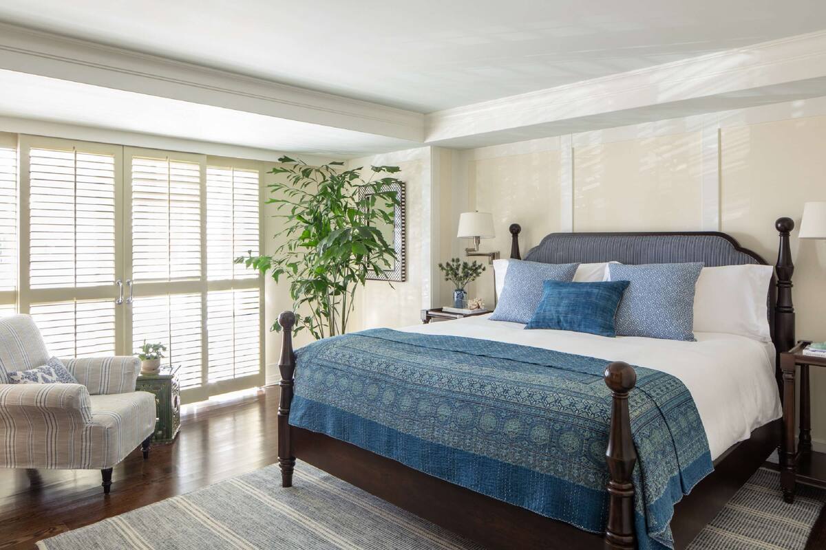 A spacious bedroom with a large bed, a chair, a nightstand, and a potted plant.