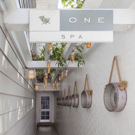 A spa corridor with a sign reading "ONE SPA," hanging plants, and rustic hanging pots.