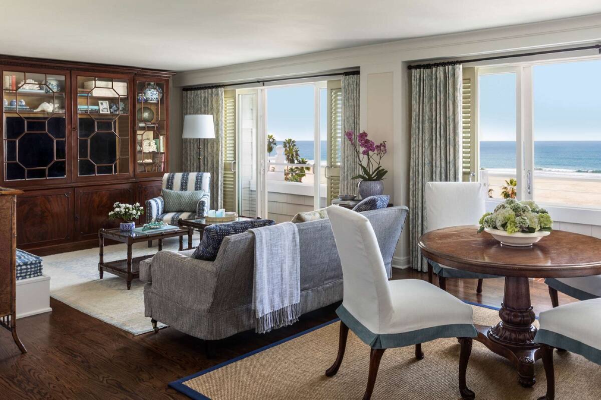 A spacious living room with a view of the beach, featuring a round wooden table, two sofas, and a cabinet with glass doors.