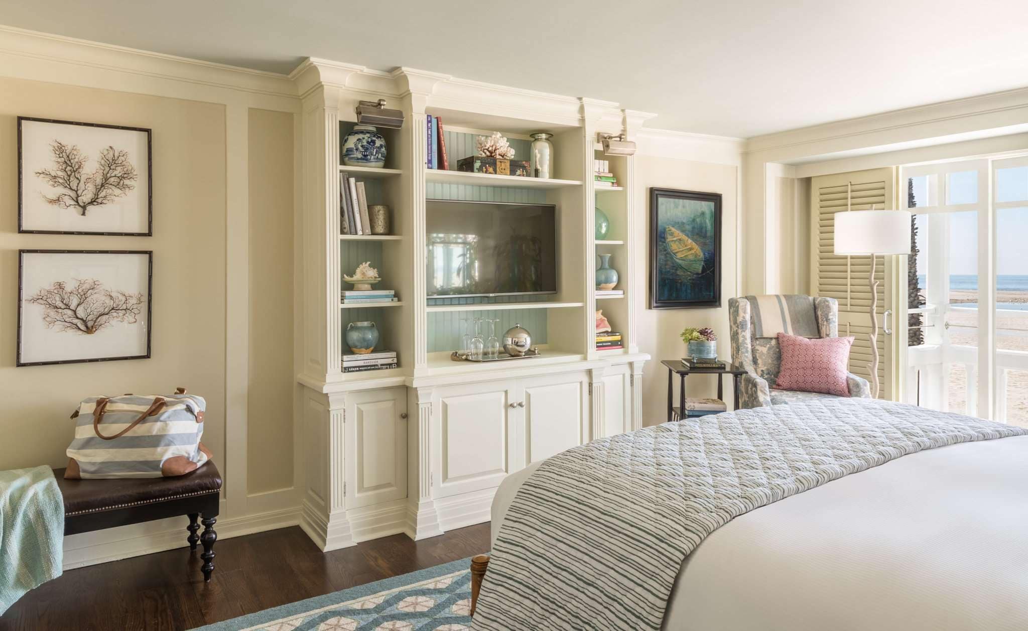 A bedroom with a large bed, a built-in bookshelf, a chair with a view, and artwork on the walls.