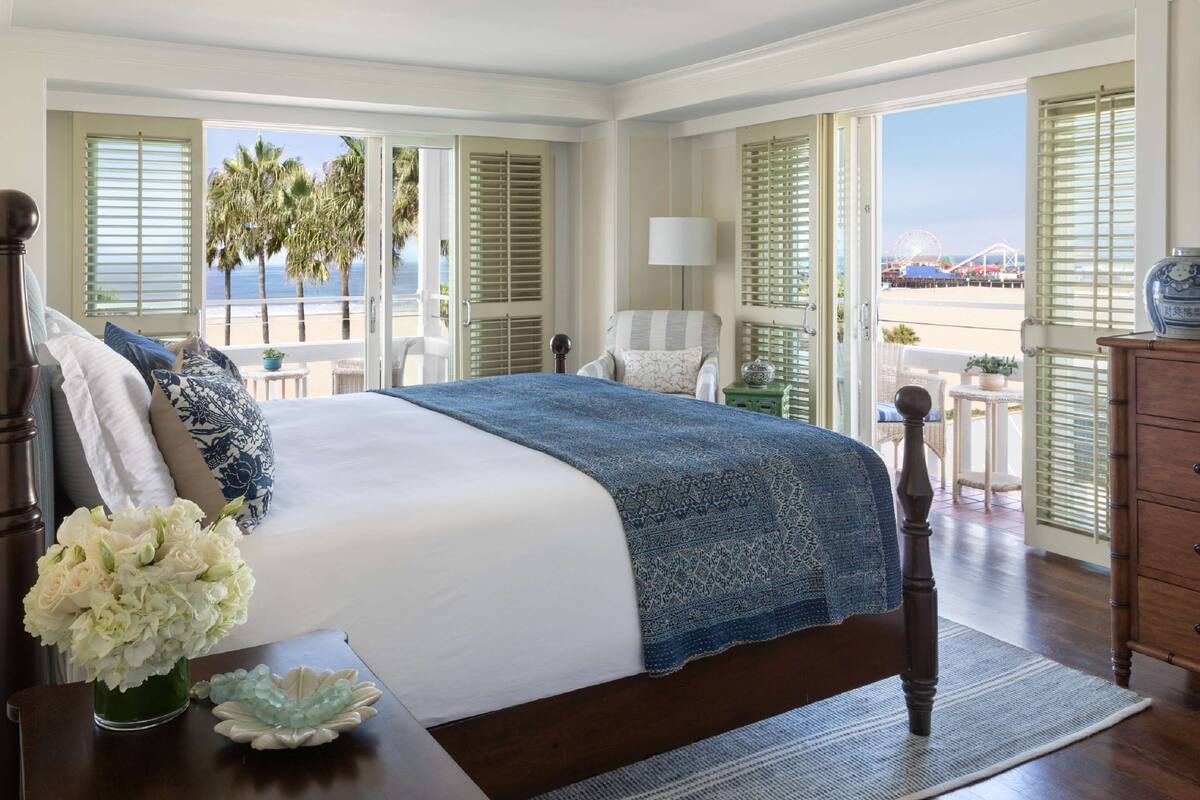 A bedroom with a large bed, a view of the beach, and a chair by the window.