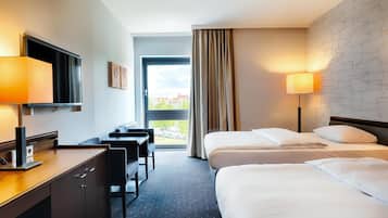 Habitación de hotel con escritorio, dos camas, televisor y ventana con cortinas.